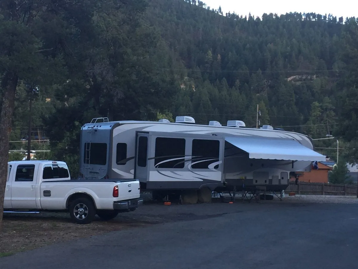 A fifth wheel lit up on its stone terrace as dusk settles over the forested ridge